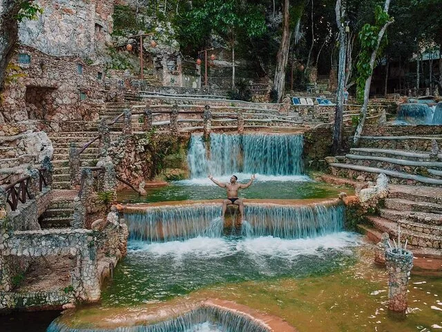 A person sitting on a small artificial waterfall with stone steps and pools around.